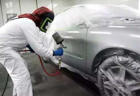Trabajador de taller de pintura de coches pintando un coche blanco con spray